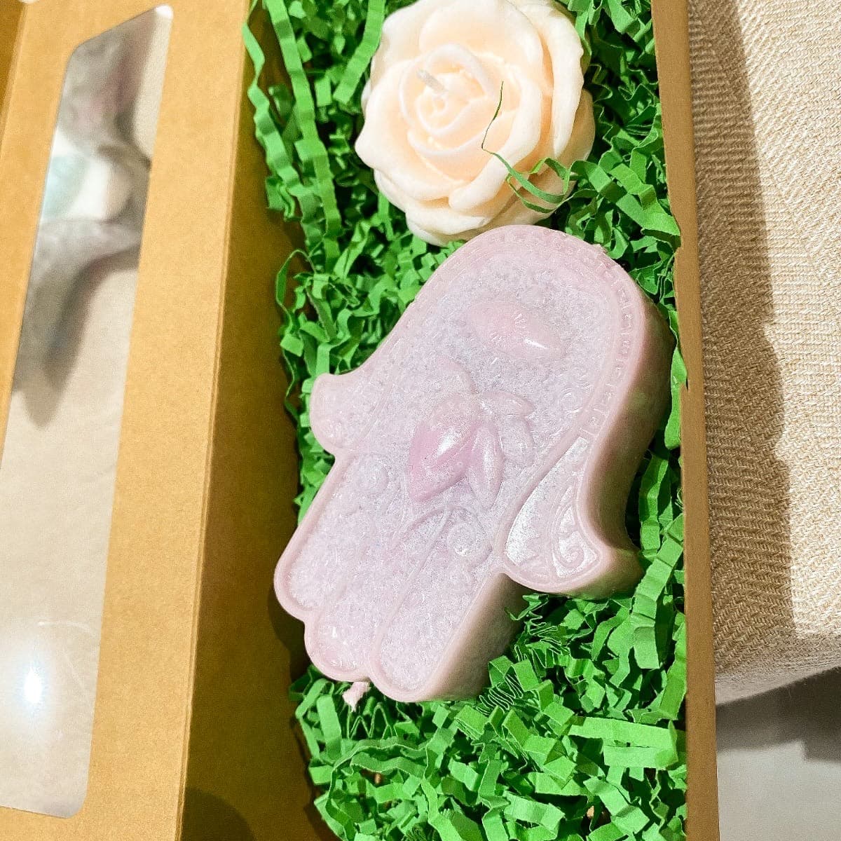 Pearly hamsa hand beside a cream rose candle in a kraft gift box