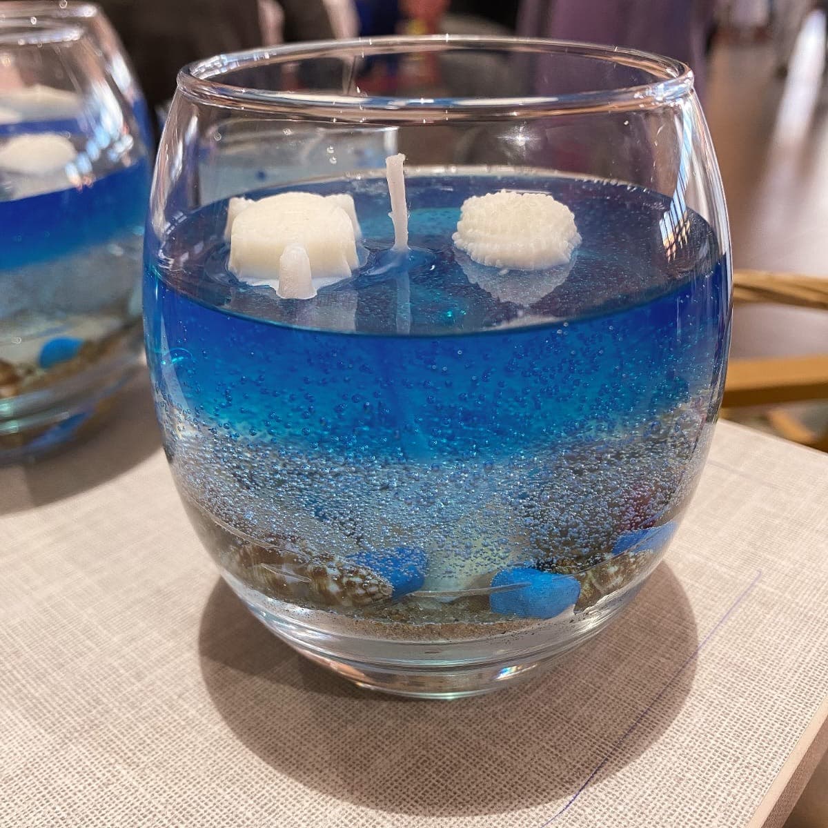 Round glass candle with deep blue gel wax, sand and shells like the sea floor